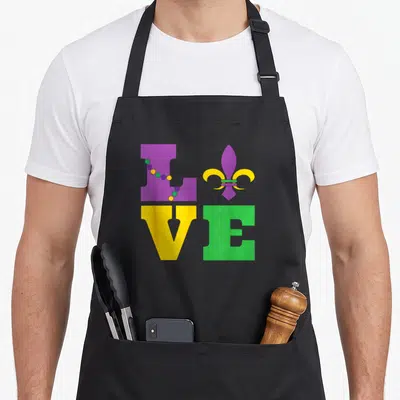 Lis fat chef apron - LOVE text in purple yellow and green grid with beads and fleur de lis symbol — shown on a black cotton canvas apron against a white background