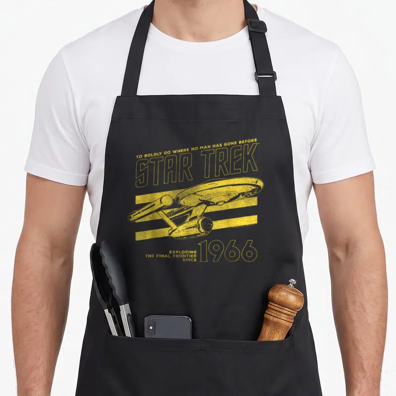 Original collegiate aprons - Yellow Star Trek Enterprise ship over three lines with 1966 text — shown on a black cotton canvas apron against a white background