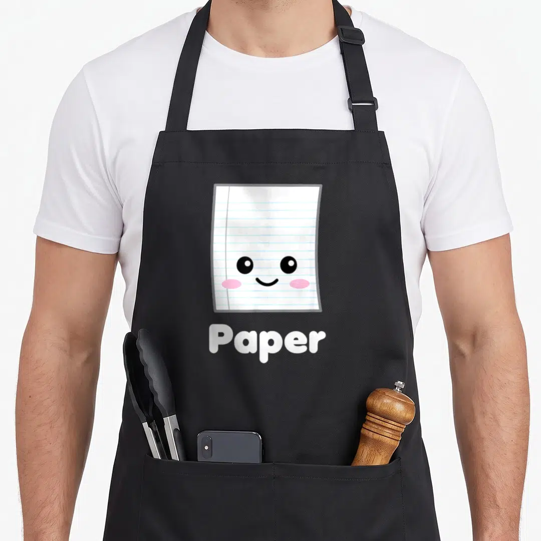 Costume paper apron - Cartoon lined paper character with smile and pink cheeks above white text reading Paper — shown on a black cotton canvas apron against a white background