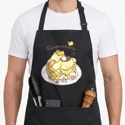 Pompompurin pancake apron - Pompompurin sitting on a white plate holding a honey jar with small animal friends — shown on a black cotton canvas apron against a white background