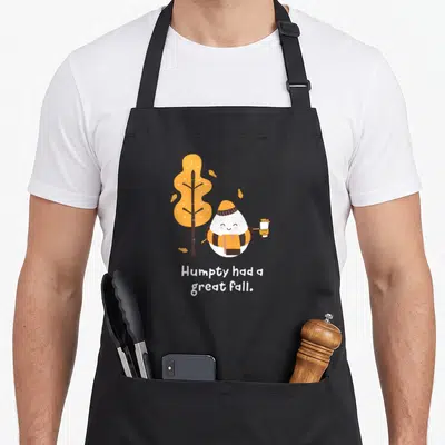 Joke cute fall aprons - Cartoon egg in hat and scarf holding cup near orange tree with white text below — shown on a black cotton canvas apron against a white background