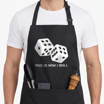 Board roll game aprons - Two white dice with black dots above white text reading THIS IS HOW I ROLL — shown on a black cotton canvas apron against a white background