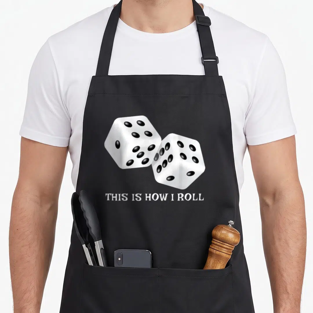 Board roll game aprons - Two white dice with black dots above white text reading THIS IS HOW I ROLL — shown on a black cotton canvas apron against a white background