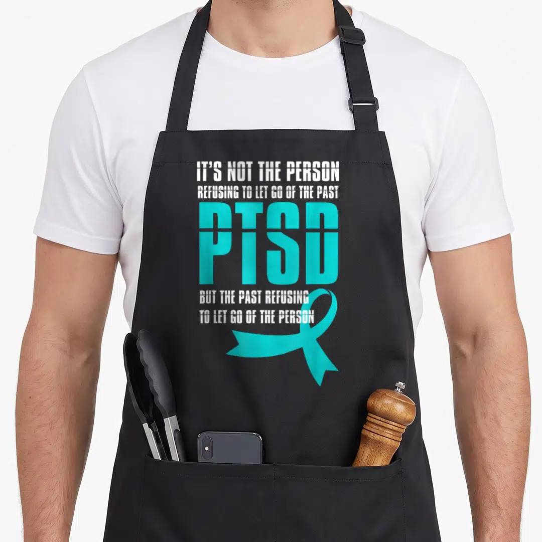 Ptsd psychology apron - Stacked white and teal PTSD text with a teal awareness ribbon overlapping the bottom line — shown on a black cotton canvas apron against a white background