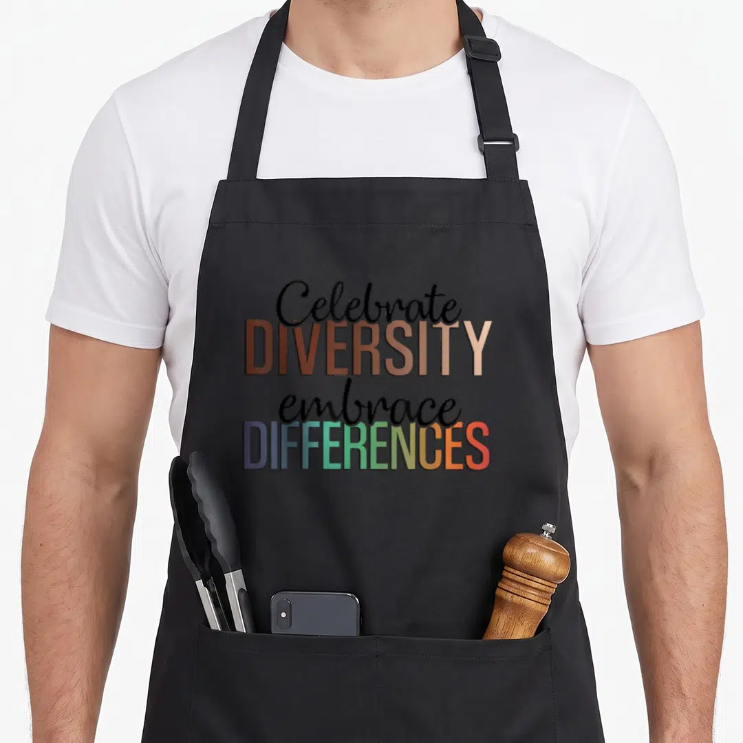 Embrace celebrate diversity apron - Stacked text reading Celebrate DIVERSITY embrace DIFFERENCES in mixed fonts — shown on a black cotton canvas apron against a white background