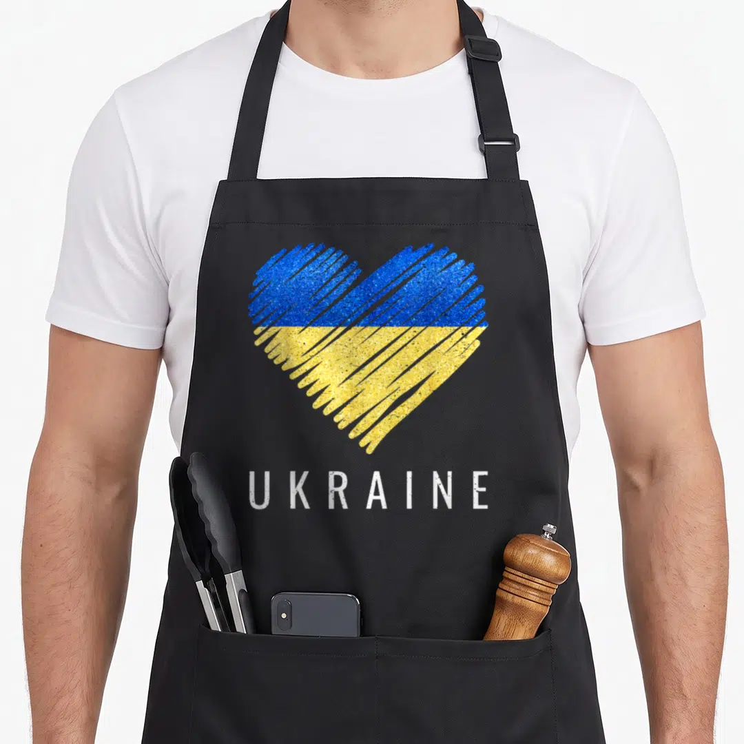 Cute flag ukrainian aprons - Scribbled blue and yellow heart above white UKRAINE text — shown on a black cotton canvas apron against a white background