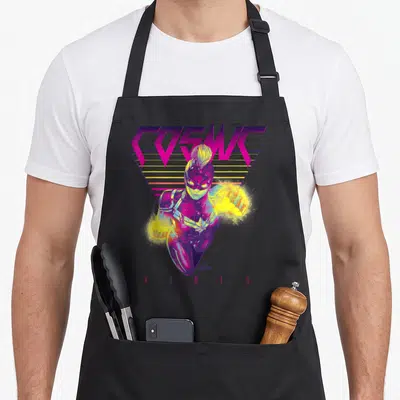 Captain triangle apron - Retro Captain Marvel illustration with COSMIC V I B E S text in purple pink and yellow striped — shown on a black cotton canvas apron against a white background