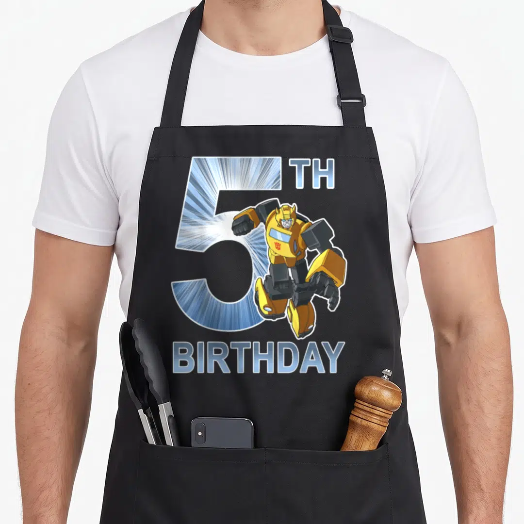 Bumblebee 5th birthday apron - Cartoon robot in yellow and blue posing before large number 5 with TH BIRTHDAY text — shown on a black cotton canvas apron against a white background