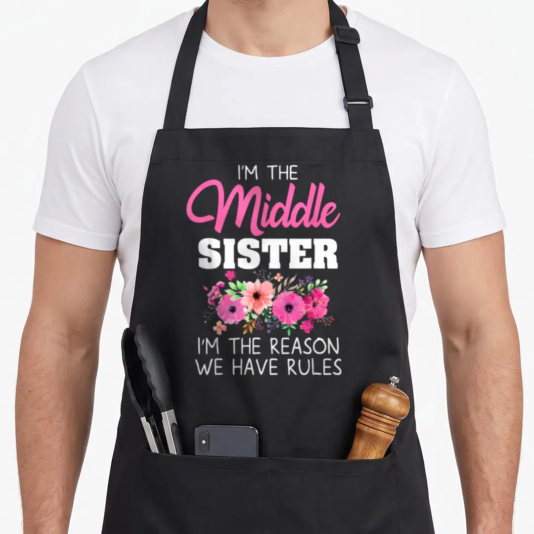 Sister middle squad apron - I'M THE Middle SISTER text with pink and green flower cluster — shown on a black cotton canvas apron against a white background
