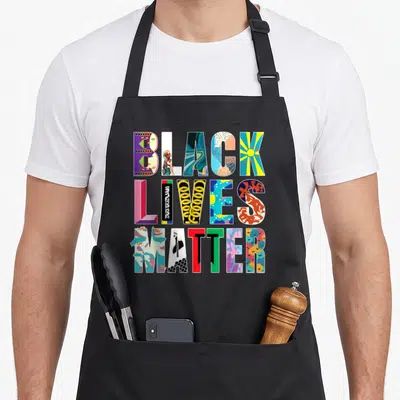 Live celebrate diversity apron - Stacked BLACK LIVES MATTER text letters filled with colorful unique illustrations — shown on a black cotton canvas apron against a white background