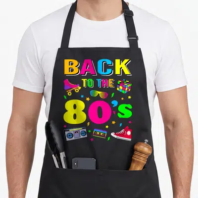 Eighty costume 80s apron - Stacked BACK TO THE 80'S text with boombox, skate, cube, glasses, tape, shoe, and stars — shown on a black cotton canvas apron against a white background