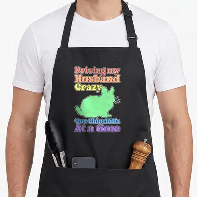 Funny chinchilla driving apron - Colorful text Driving my Husband Crazy One Chinchilla At a time surrounding a light — shown on a black cotton canvas apron against a white background