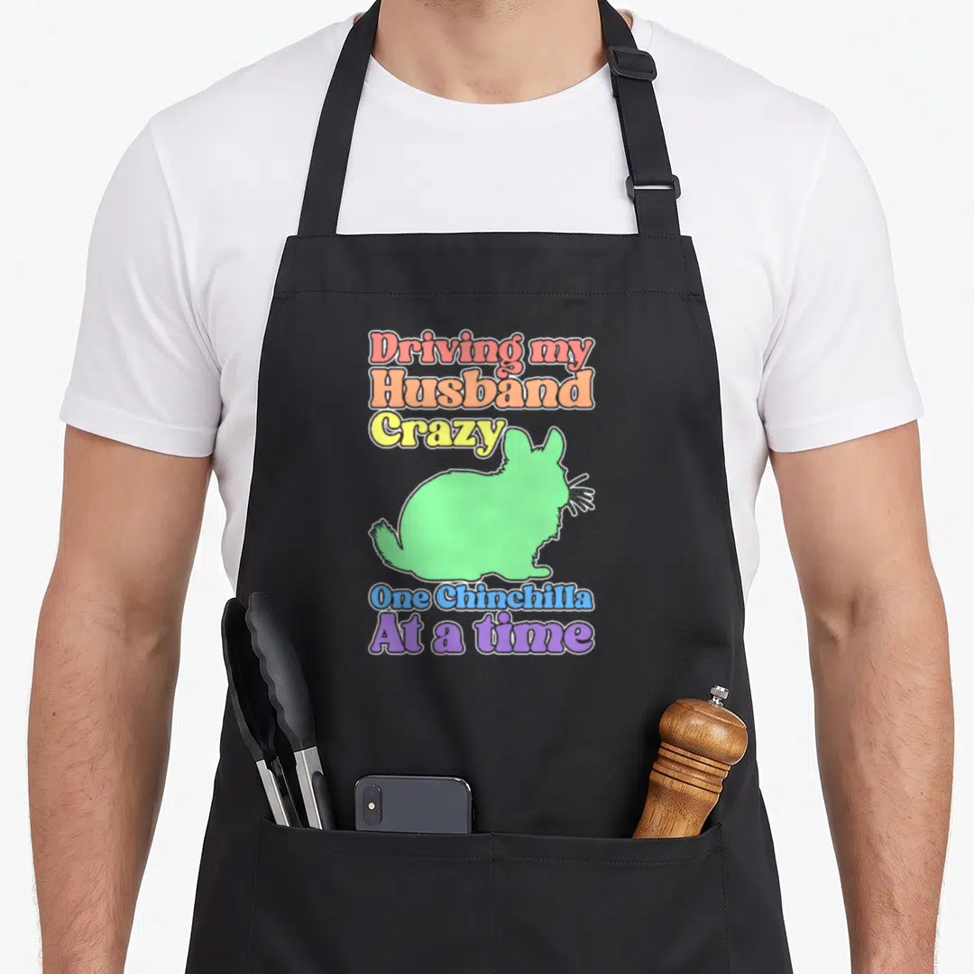 Funny chinchilla driving apron - Colorful text Driving my Husband Crazy One Chinchilla At a time surrounding a light — shown on a black cotton canvas apron against a white background