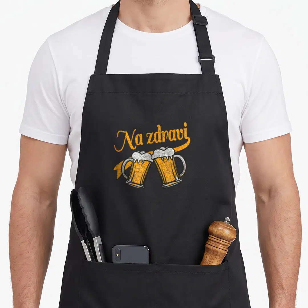 Czech beer apron - Na zdravi script above two clinking beer mugs on yellow banner — shown on a black cotton canvas apron against a white background