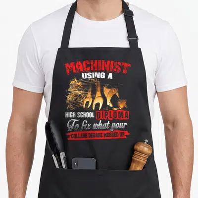 Power mechanic apron - Machinist high school diploma text above sparks and wrench graphic with red brushstroke — shown on a black cotton canvas apron against a white background