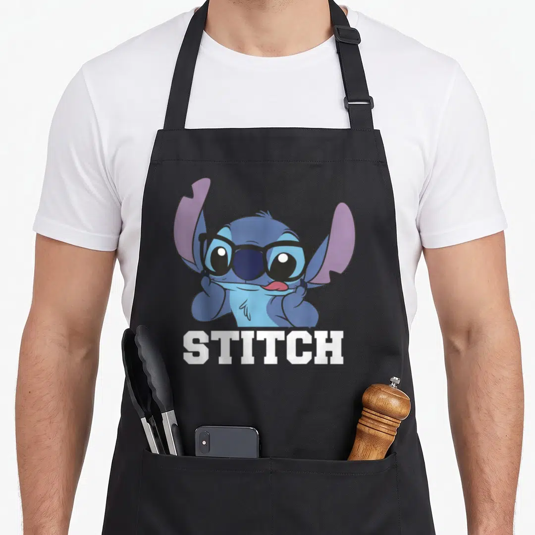 Nerdy stitch apron - Blue cartoon character wearing black glasses with white STITCH text below — shown on a black cotton canvas apron against a white background