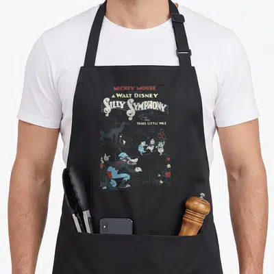 Present silly apron - Big Bad Wolf and three pigs cartoon art with stacked Silly Symphony title text — shown on a black cotton canvas apron against a white background