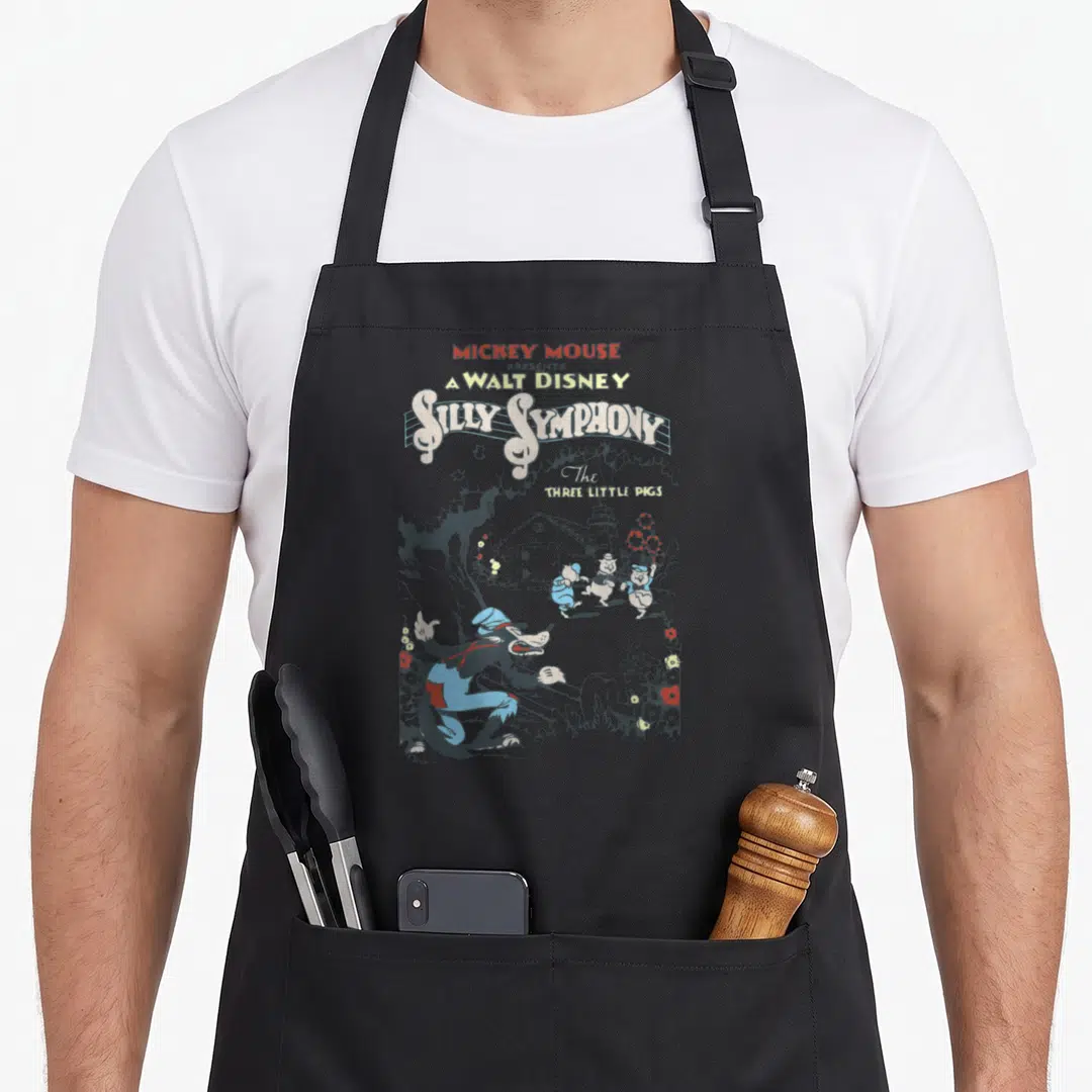 Present silly apron - Big Bad Wolf and three pigs cartoon art with stacked Silly Symphony title text — shown on a black cotton canvas apron against a white background