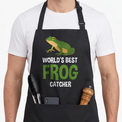 Catcher frog aprons - Green cartoon frog above white and green text reading WORLD'S BEST FROG CATCHER — shown on a black cotton canvas apron against a white background