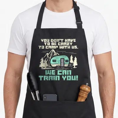 Van camping apron - Retro camper trailer between trees with mint and white text reading You Don't Have To Be Crazy — shown on a black cotton canvas apron against a white background