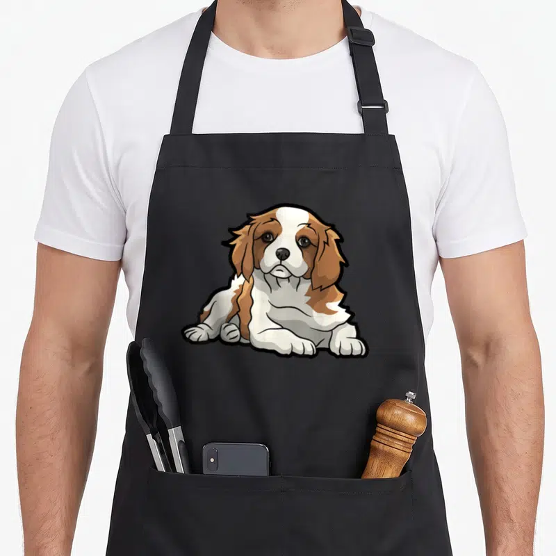 Puppy king apron - Cartoon Blenheim Cavalier King Charles Spaniel puppy in brown, white, and black — shown on a black cotton canvas apron against a white background