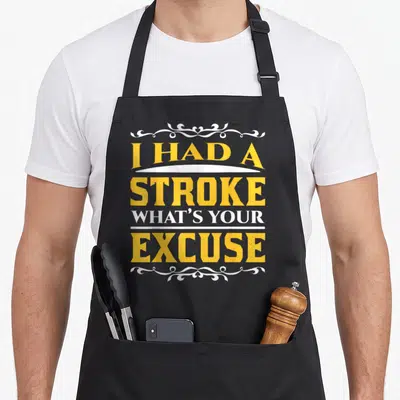 Excuse stroke awareness apron - Yellow and white typography reading I had a stroke what's your excuse with decorative — shown on a black cotton canvas apron against a white background