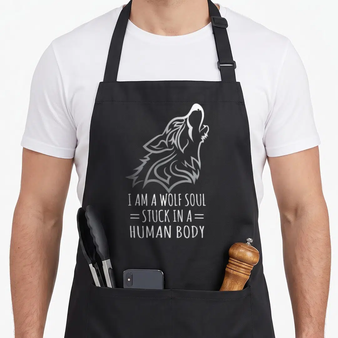 Wolf human body apron - Stylized grey wolf head above white text reading I AM A WOLF SOUL STUCK IN A HUMAN BODY — shown on a black cotton canvas apron against a white background