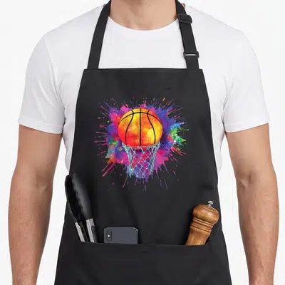 Basketball drip colorful aprons - Watercolor basketball falling into a hoop over orange, blue, and purple splatter — shown on a black cotton canvas apron against a white background