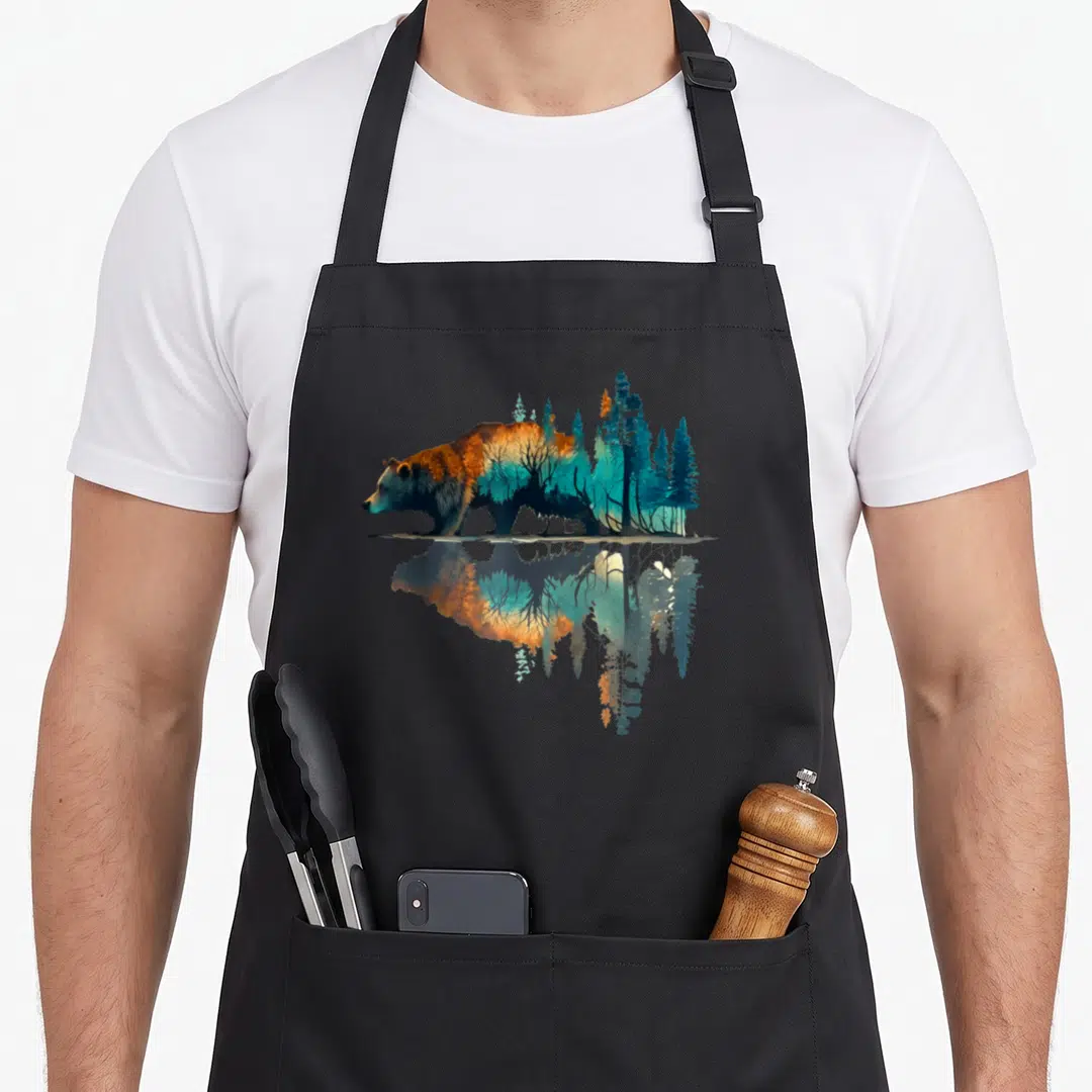 Reflection bear apron - Bear silhouette filled with blue and orange forest trees mirrored in water reflection — shown on a black cotton canvas apron against a white background