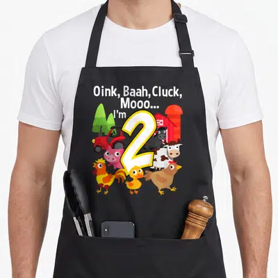 Barn farm aprons - Cartoon number 2 with farm animals and barn background under animal sound text — shown on a black cotton canvas apron against a white background