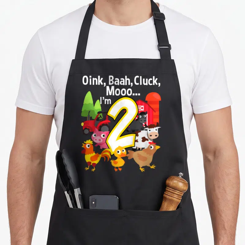 Barn farm aprons - Cartoon number 2 with farm animals and barn background under animal sound text — shown on a black cotton canvas apron against a white background