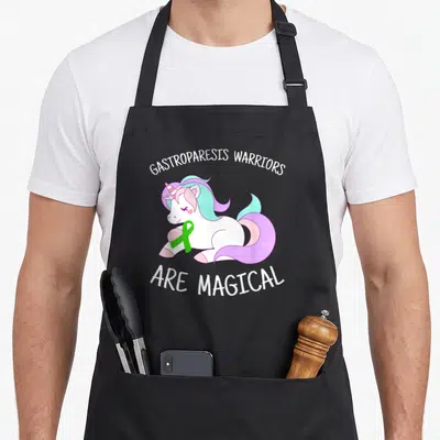 Gastroparesis unicorn apron - White unicorn holding green ribbon with text warriors are magical in cartoon style — shown on a black cotton canvas apron against a white background