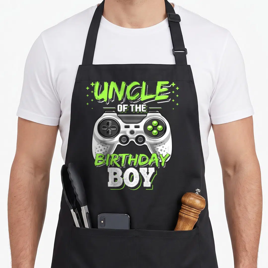 Uncle birthday video game apron - Cartoon controller with UNCLE OF THE BIRTHDAY BOY text in lime and white — shown on a black cotton canvas apron against a white background