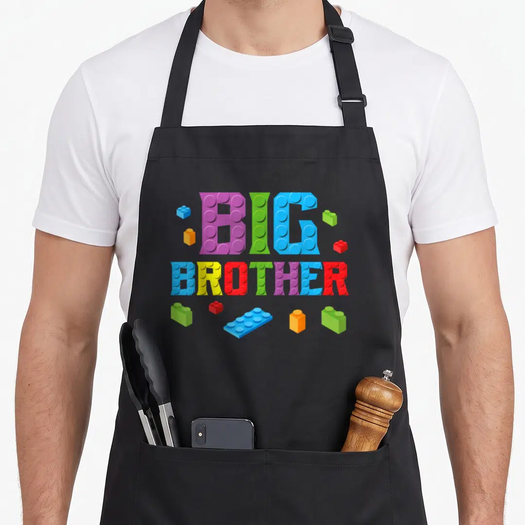 Brother block & apron - BIG BROTHER text in brick style with purple green blue yellow red toy blocks scattered around — shown on a black cotton canvas apron against a white background