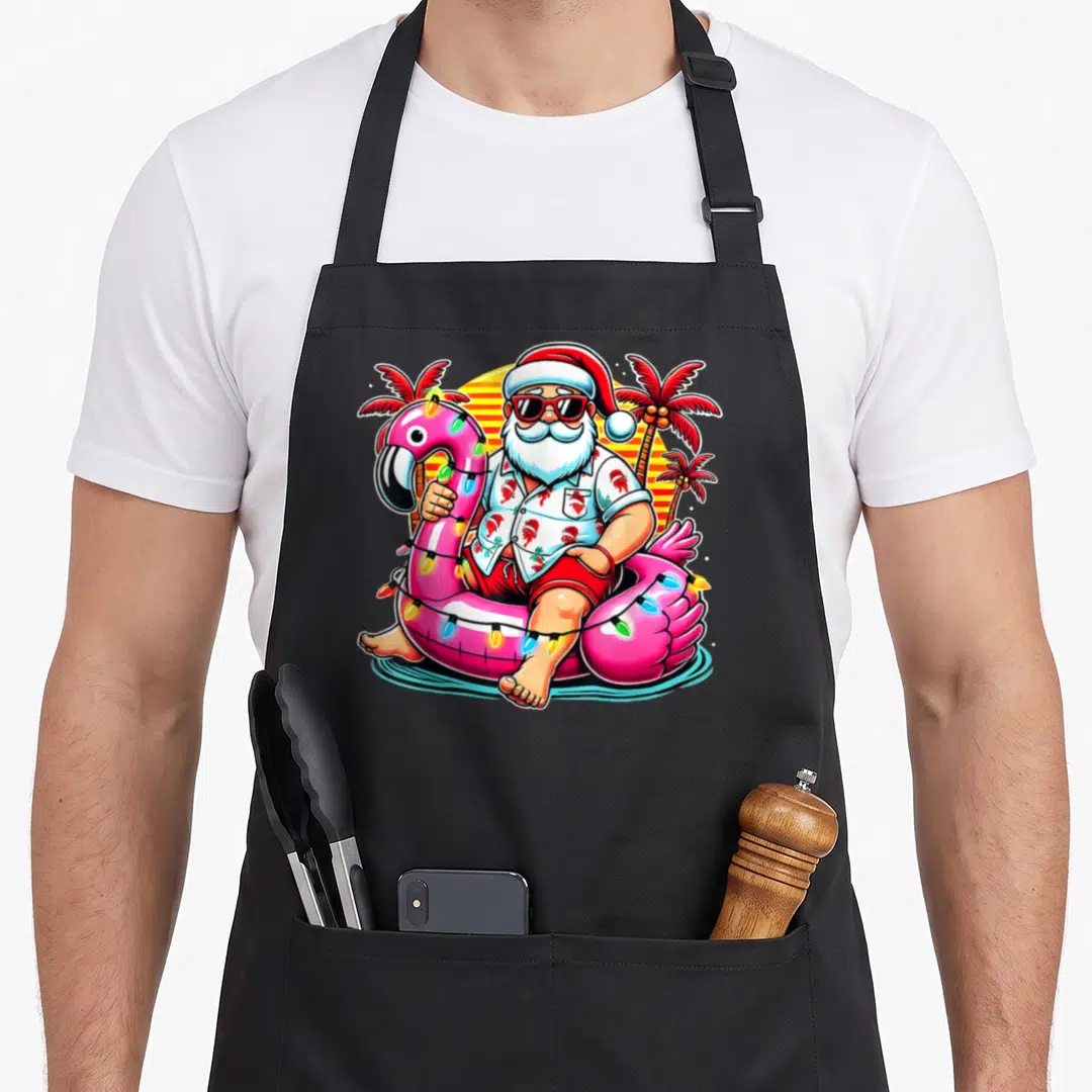 Flamingo christmas santa apron - Cartoon Santa in pink flamingo float with striped sun and two palm trees — shown on a black cotton canvas apron against a white background