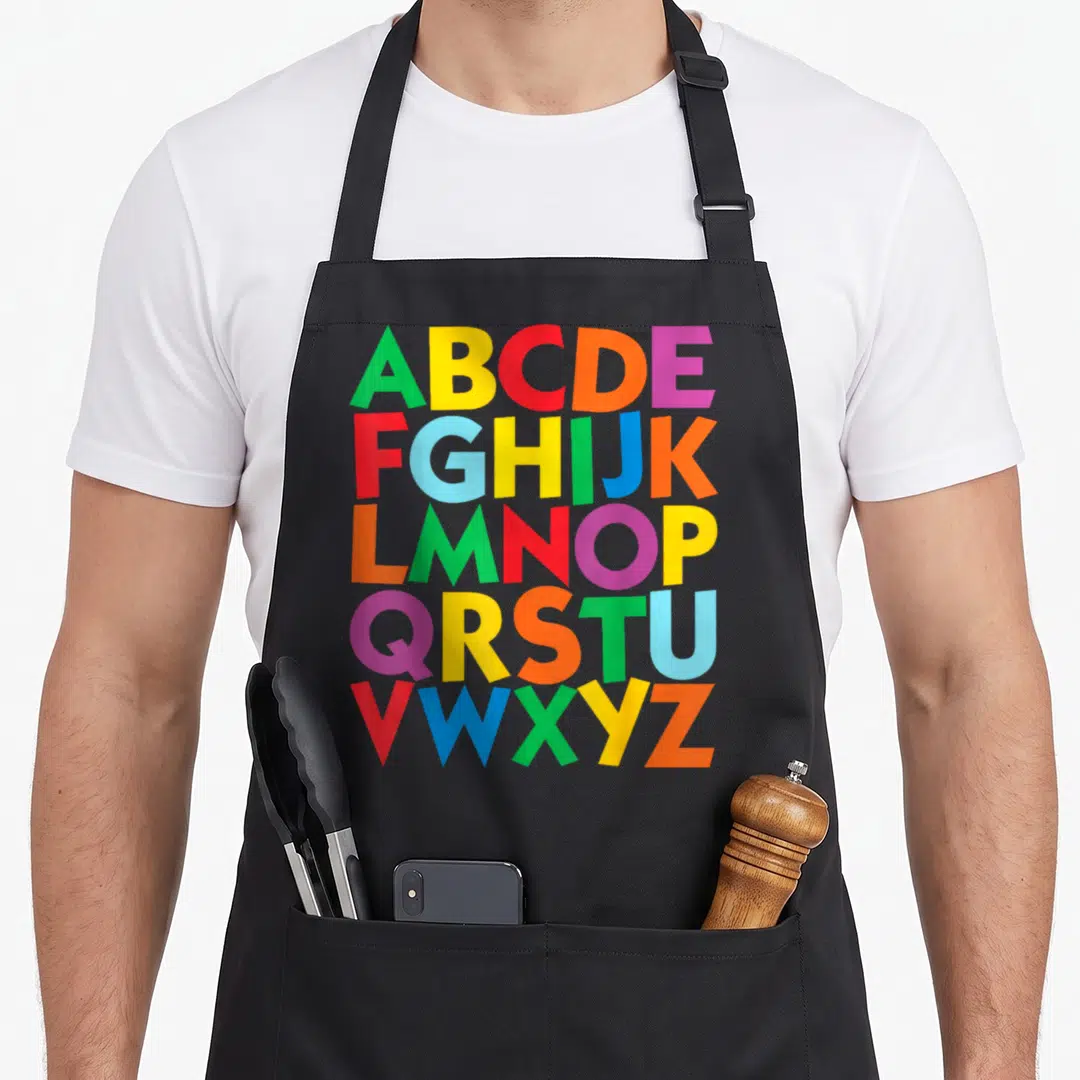 Uppercase colorful aprons - Uppercase alphabet ABCDEFGHIJKLMNOPQRSTUVWXYZ in red yellow blue green purple orange — shown on a black cotton canvas apron against a white background