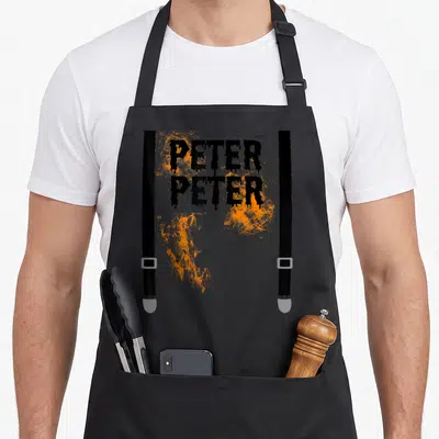 Pumpkin eater couple halloween apron - Peter Peter text over orange splatters framed by two black suspender straps — shown on a black cotton canvas apron against a white background