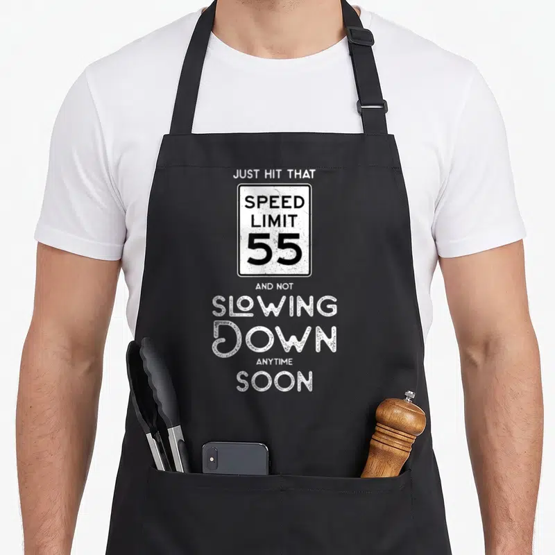 55th driving apron - Distressed speed limit 55 sign with text just hit that and not slowing down anytime soon — shown on a black cotton canvas apron against a white background