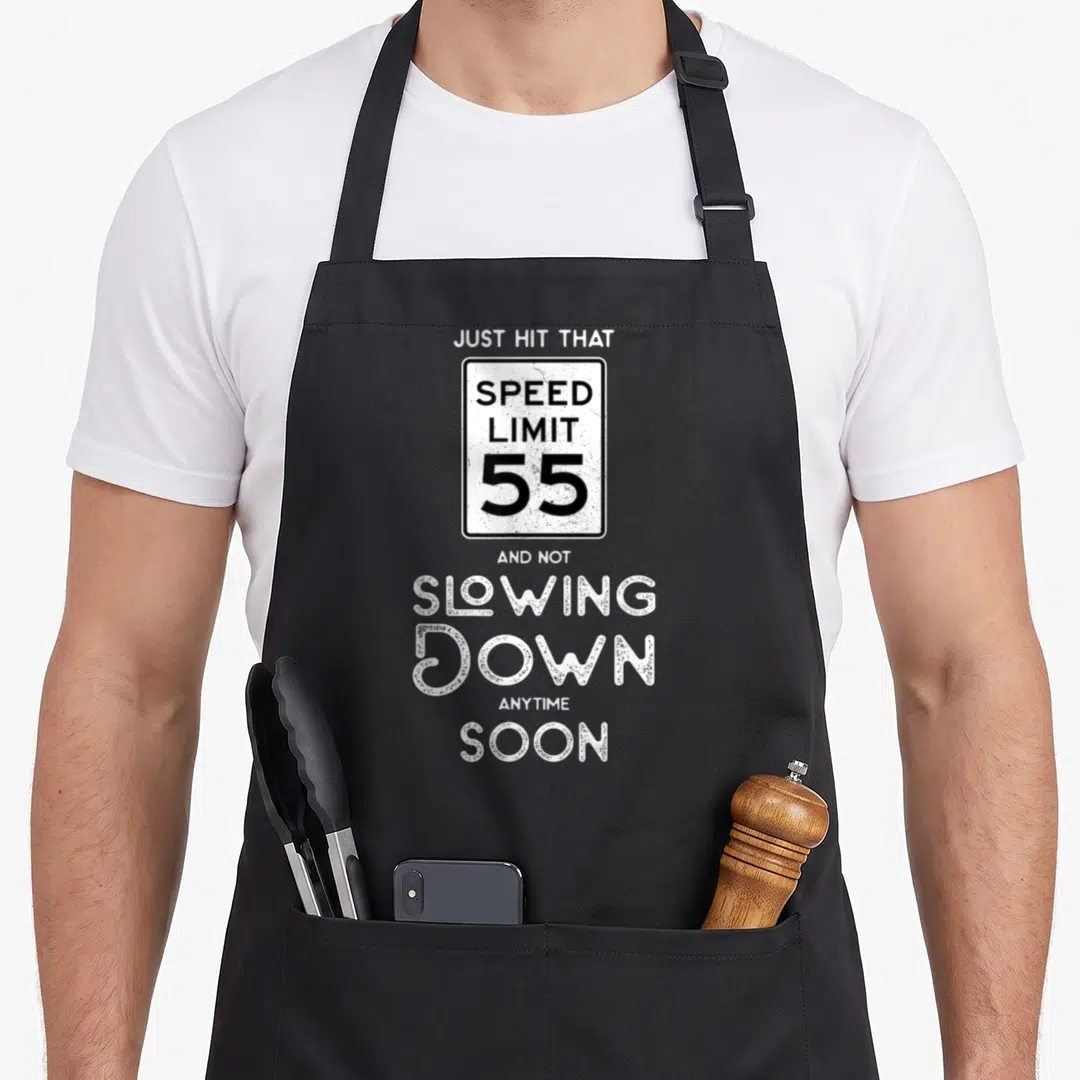 55th driving apron - Distressed speed limit 55 sign with text just hit that and not slowing down anytime soon — shown on a black cotton canvas apron against a white background
