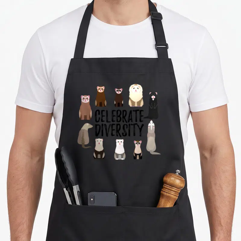 Celebrate ferret lover apron - Ten cartoon ferrets in black, brown, and white surrounding CELEBRATE DIVERSITY text — shown on a black cotton canvas apron against a white background