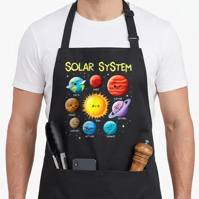 Solar teacher apron - Cartoon sun and planets Earth Mars Jupiter Venus Saturn Mercury Neptune Uranus with names below — shown on a black cotton canvas apron against a white background