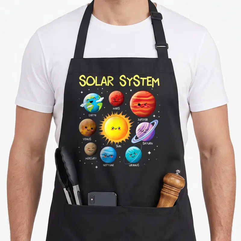 Solar teacher apron - Cartoon sun and planets Earth Mars Jupiter Venus Saturn Mercury Neptune Uranus with names below — shown on a black cotton canvas apron against a white background