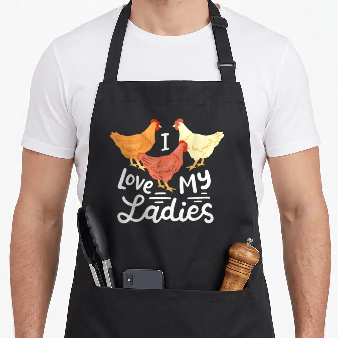 Vintage farmer animal chicken apron - Three cartoon chickens in orange, red, and cream surrounding white text reading I — shown on a black cotton canvas apron against a white background