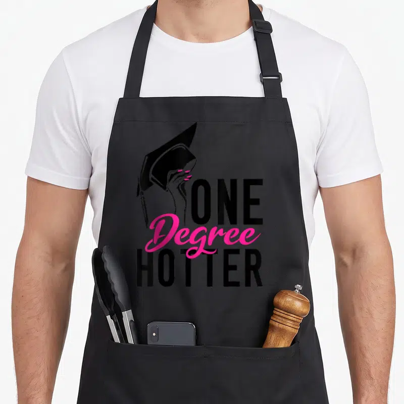 Degree school graduation apron - Black hand holds cap beside pink Degree text flanked by black ONE and HOTTER — shown on a black cotton canvas apron against a white background