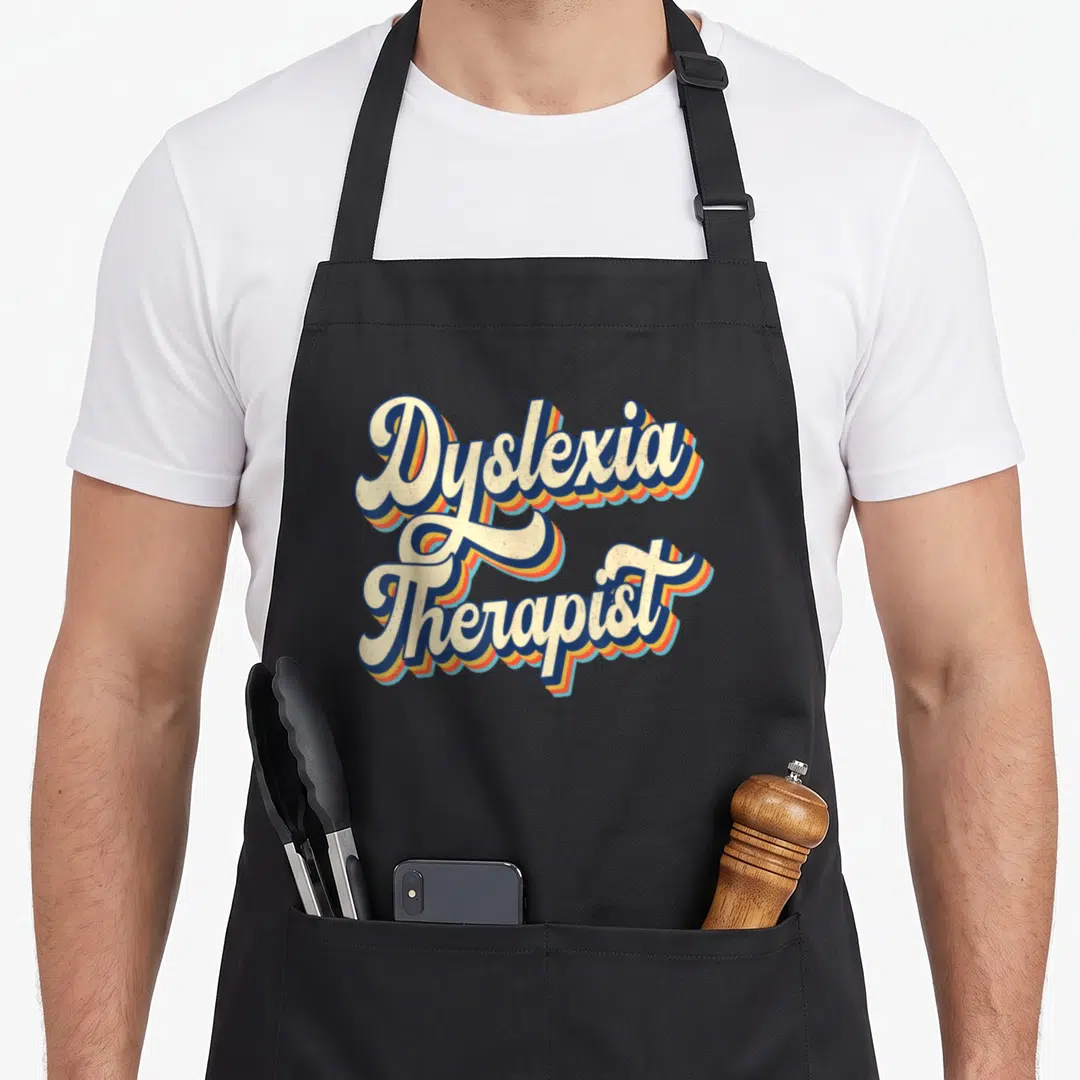 Dyslexia my therapy apron - Retro script text Dyslexia Therapist with blue orange and yellow 3D shadow layers — shown on a black cotton canvas apron against a white background
