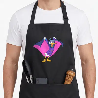 Funny darkwing duck apron - Centered cartoon duck in purple coat and pink-lined cape holding hat — shown on a black cotton canvas apron against a white background