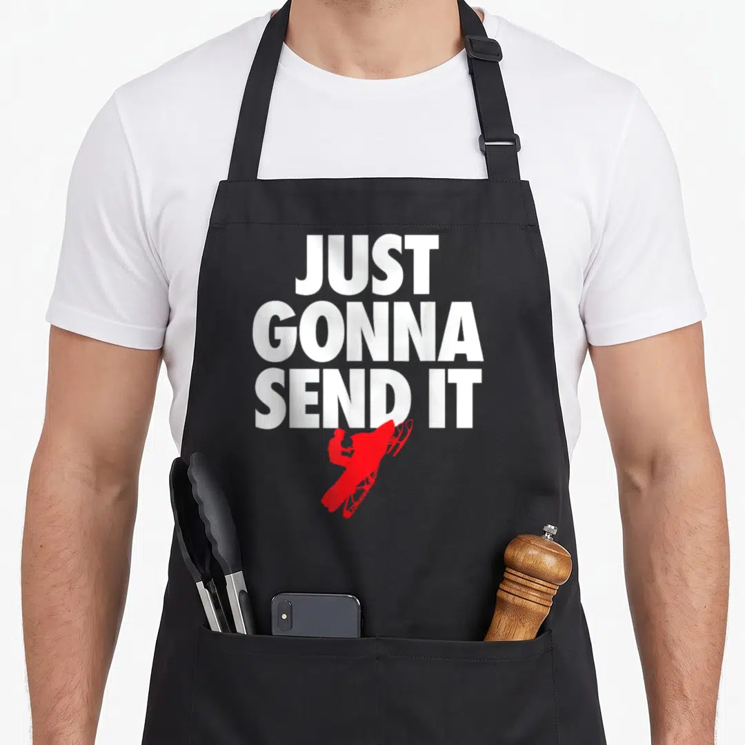 Send snowmobile girl apron - Just Gonna Send It text above red snowmobile rider silhouette — shown on a black cotton canvas apron against a white background
