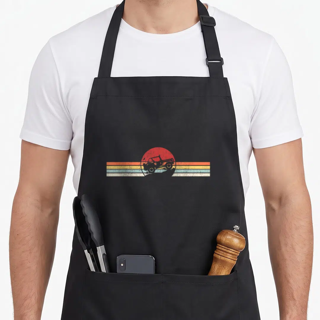 Funny 4x4 road apron - Grey off-road vehicle over red sun and four horizontal stripes in orange, yellow, light blue — shown on a black cotton canvas apron against a white background