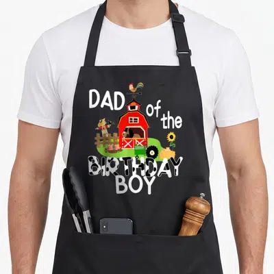 Barnyard farm aprons - Red barn with horse pig rooster and cow print text reading Dad of the Birthday Boy — shown on a black cotton canvas apron against a white background
