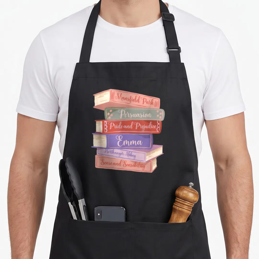 Literacy jane austen apron - Six stacked books withJane Austen novel titles on spines in pink, green, red, purple — shown on a black cotton canvas apron against a white background
